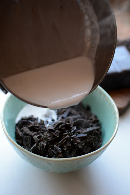 Chopped dark chocolate in a bowl with hot milk being poured over the top.