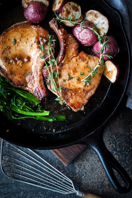 pork chops in a skillet with fresh thyme and red potatoes
