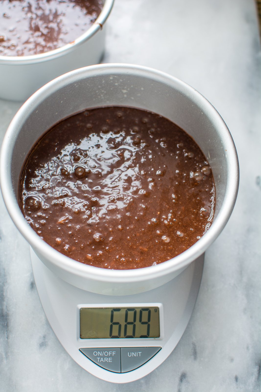 Chocolate cake batter in round cake pan on a scale