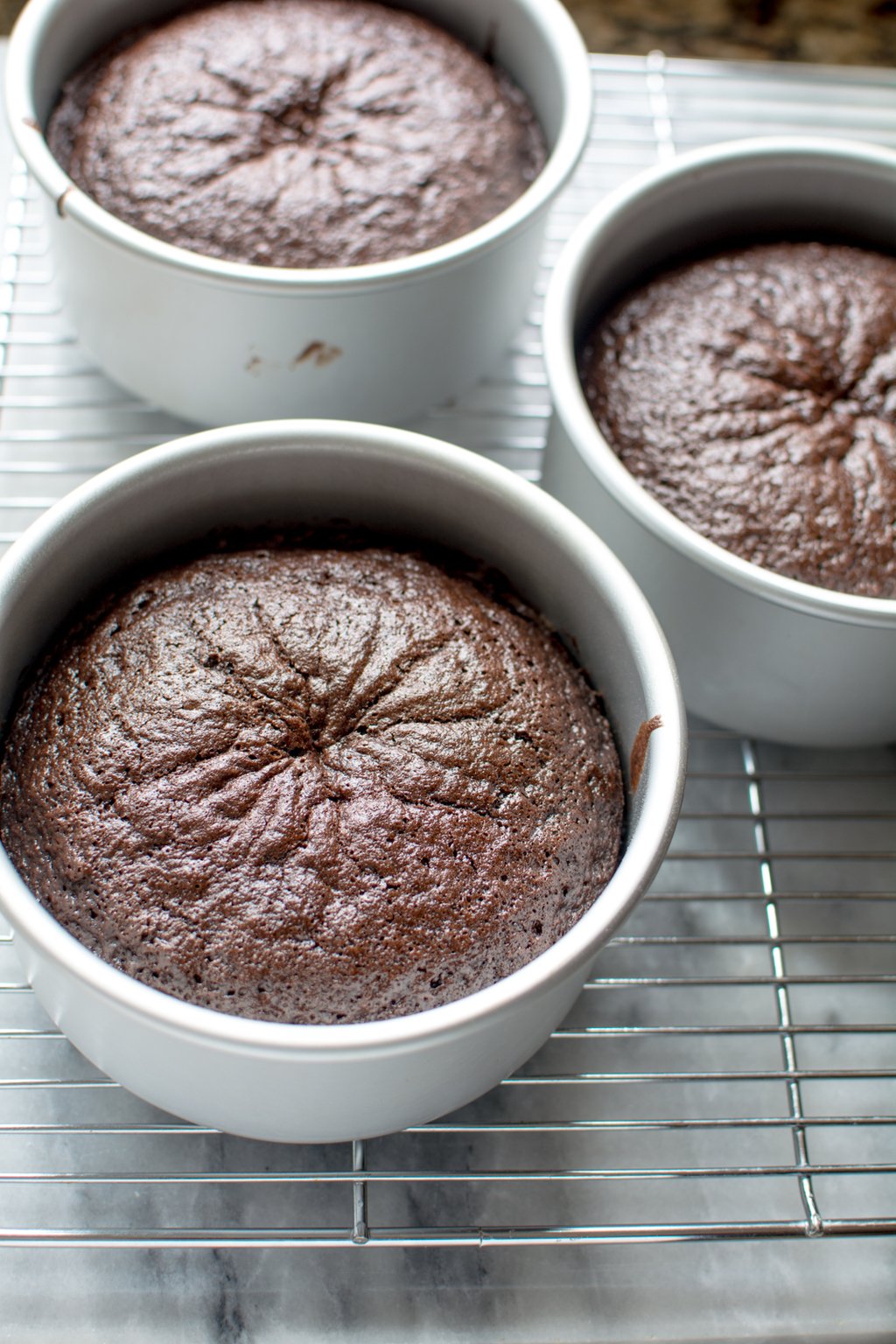 Three round baked chocolate cakes on cooling rack