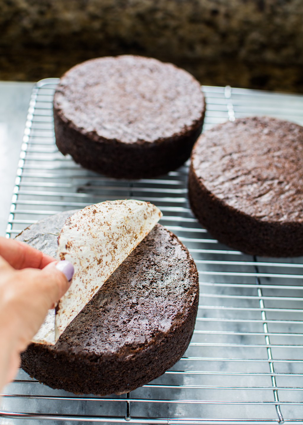 three round chocolate cakes upside down on a cooling rack parchment peeled off