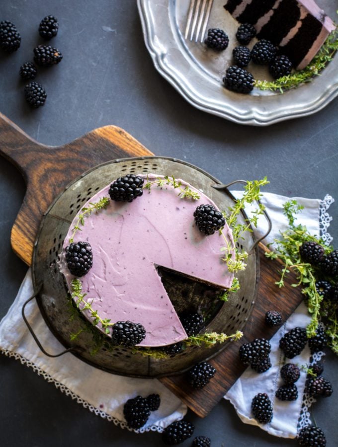 Overhead shot of Chocolate Zucchini Cake with Blackberry Buttercream on a board with blackberries and fresh thyme