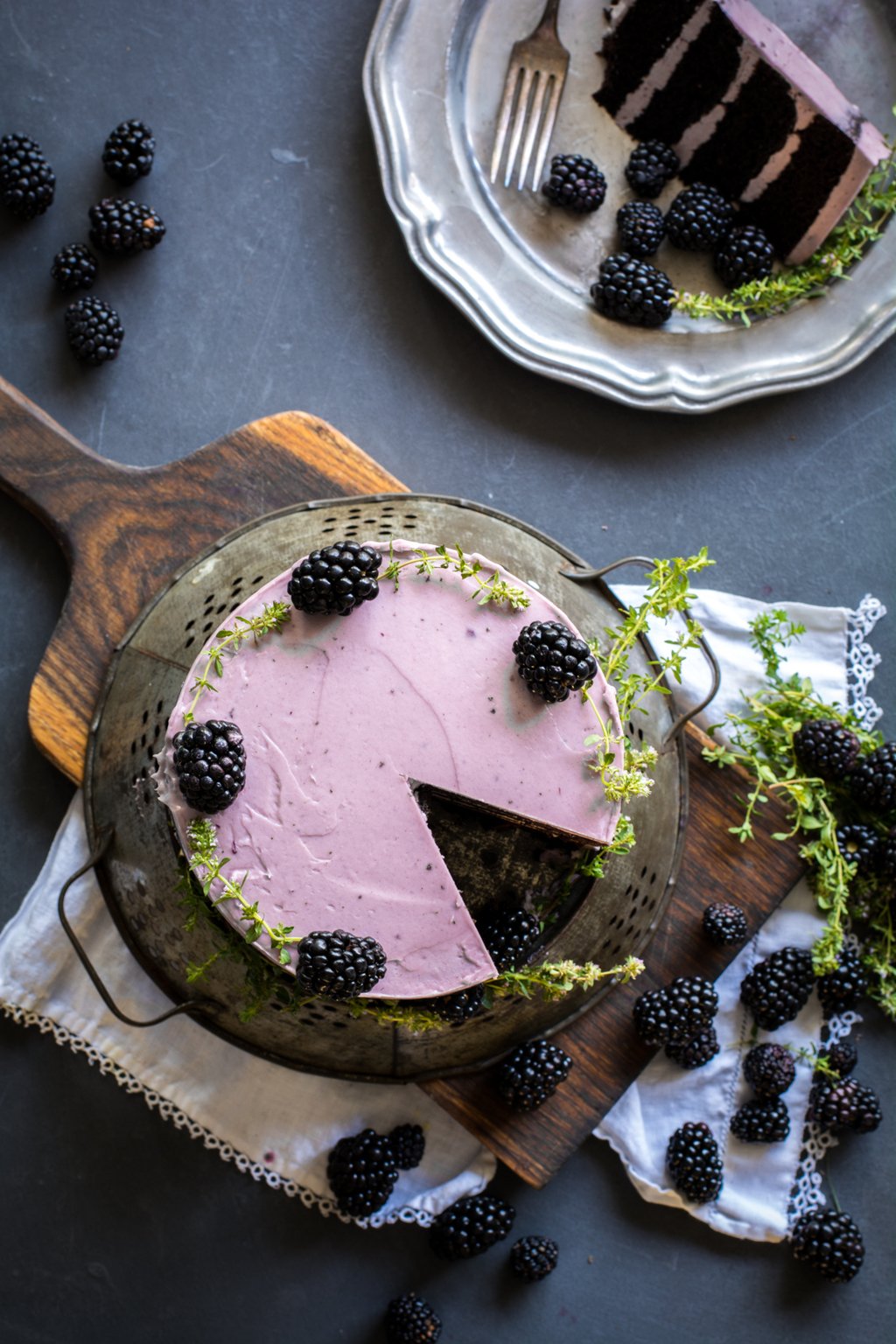 Overhead shot of Chocolate Zucchini Cake with Blackberry Buttercream on a board with blackberries and fresh thyme