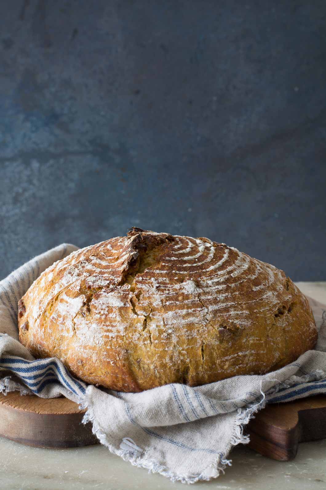 o-Knead Pumpkin Pecan Bread sitting on a bread board under a cloth