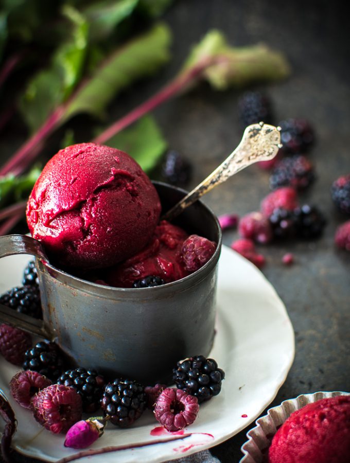 Beet Raspberry Rose Sorbet in a metal mug on a white plate with berries scatter