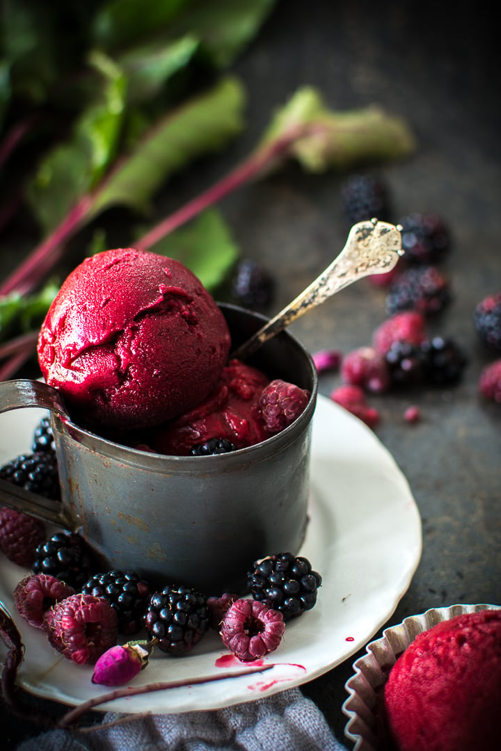 Beet Raspberry Rose Sorbet in a metal mug on a white plate with berries scatter