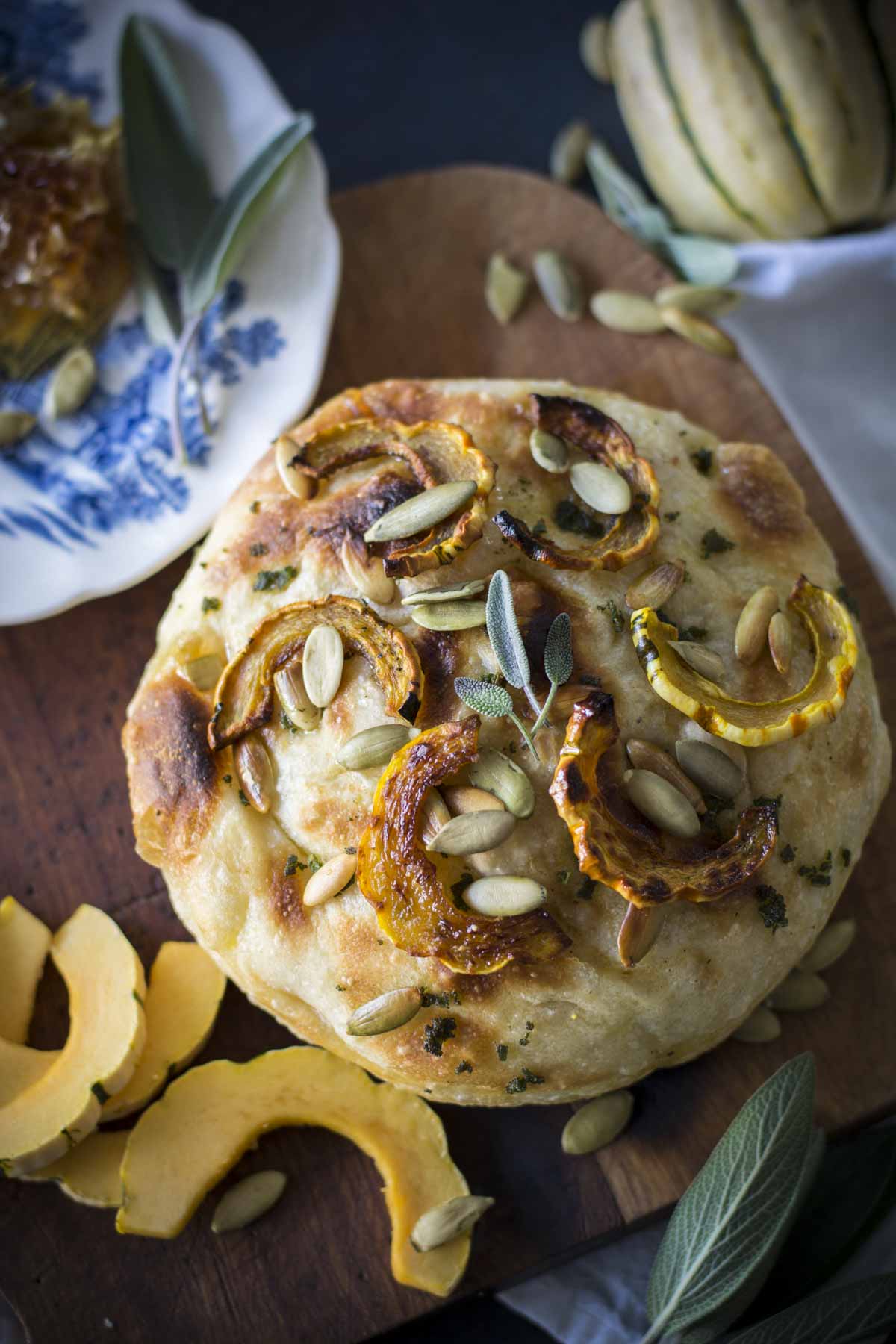 No-knead Delicata sage focaccia on cutting board with honey comb in background and slices of squash