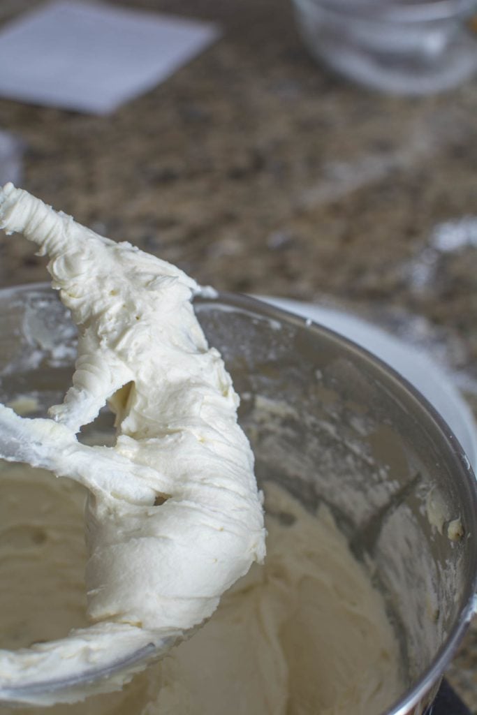 Fluffy buttercream icing in a metal bowl, mixer paddle in the bowl.