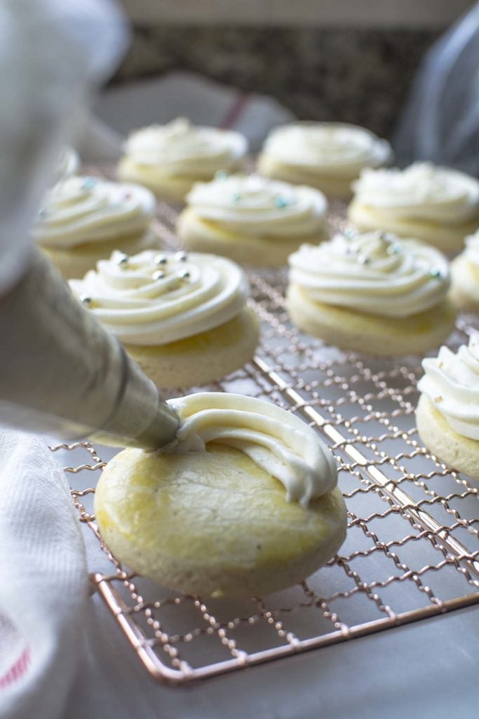 Piping buttercream frosting onto a cooled sugar cookie.