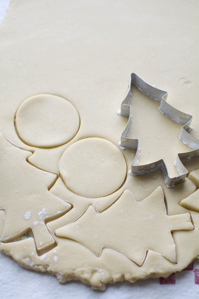 Metal Christmas tree cookie cutter, stamping out cookies on a sheet of flat dough.
