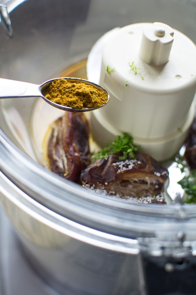 Food processor bowl with dates and a spoonful of curry powder