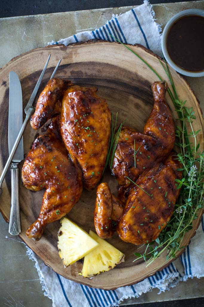 Grilled Huli Huli Chicken on a wooden platter with fresh herbs and pineapple wedges