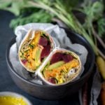 Beet, Peach, and Avocado Wrap with Turmeric Tahini Sauce cut in half in a black bowl