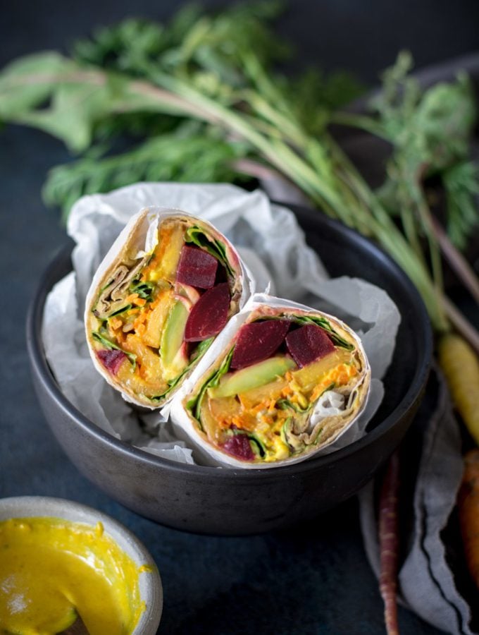 Beet, Peach, and Avocado Wrap with Turmeric Tahini Sauce cut in half in a black bowl