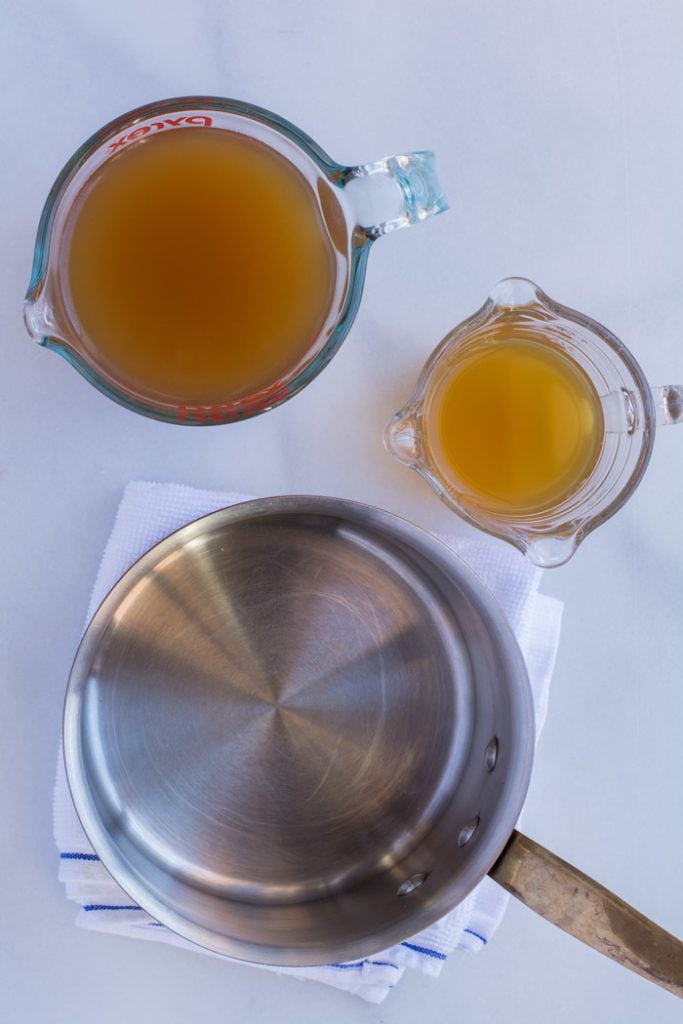 Glass cup of stock, glass cup of apple cider vinegar, and an empty stock pot.