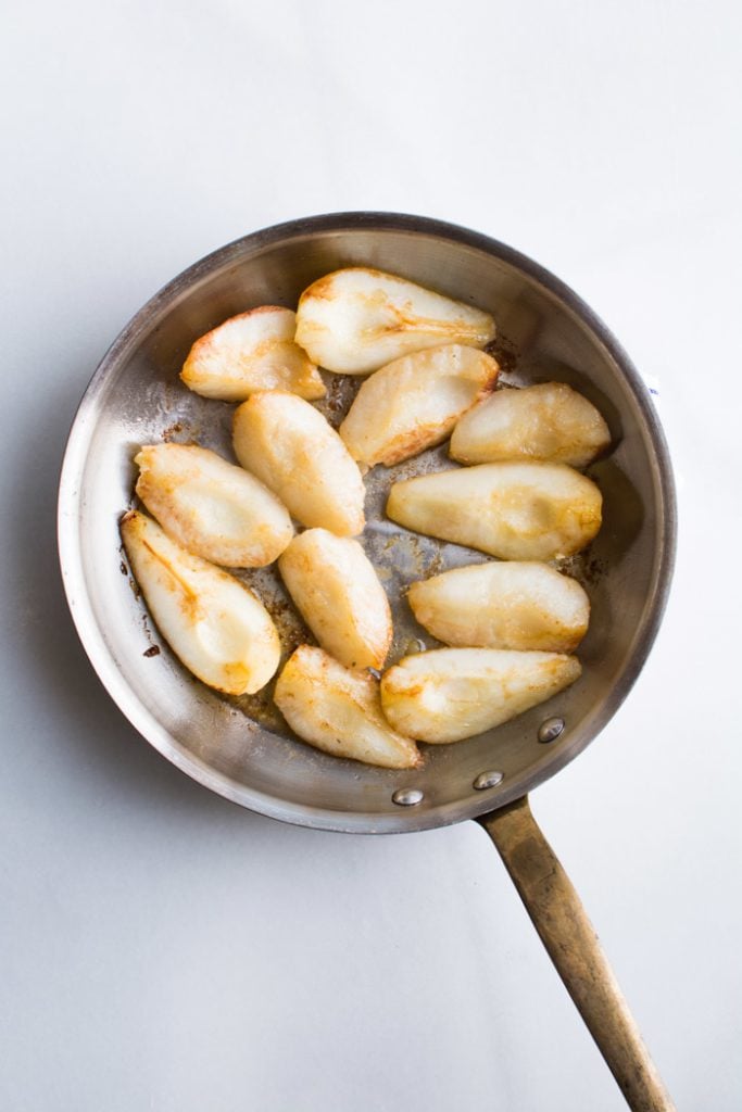 Slices of pears browning in butter in a saute pan.