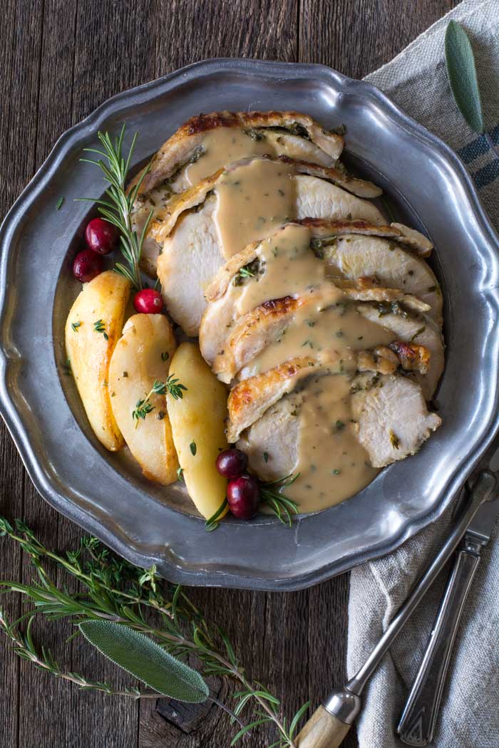 Slow cooker boneless turkey breast with fresh herb butter resting on a serving platter, cut into slices and served with brown butter pears and apple cider gravy.