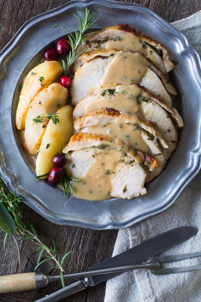 Crockpot boneless turkey breast with fresh herb butter resting on a serving platter, cut into slices and served with brown butter pears and apple cider gravy.