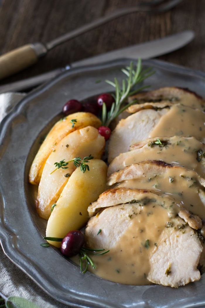 Crock pot boneless turkey breast with fresh herb butter resting on a serving platter, cut into slices and served with brown butter pears and apple cider gravy.