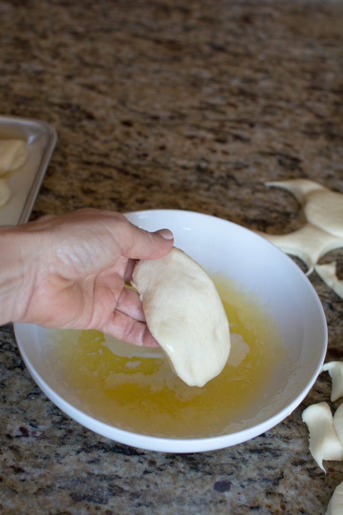 Hand holding a circular piece of dough over a bowl of melted butter.