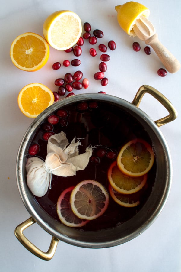 Cranberry wassail in a pot with scattered cranberries, orange slices