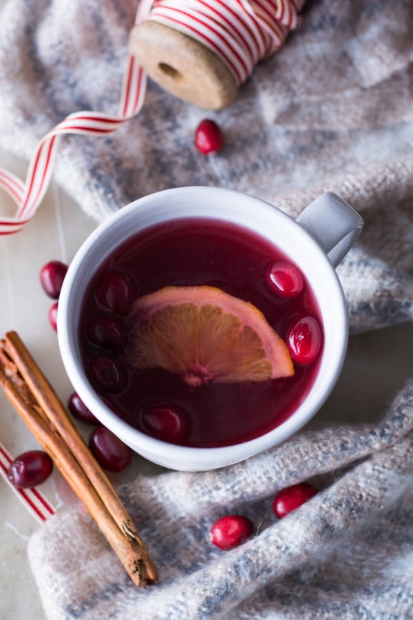 cranberry wassail in a white mug with floating orange slice and cinnamon stick