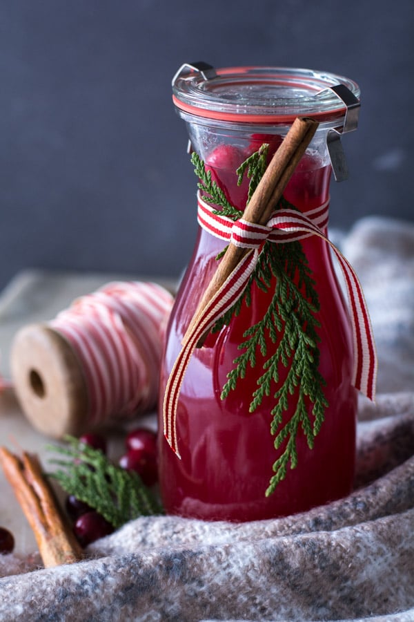 Cranberry wassail in a jar with spool of ribbon in background and cinnamon stick