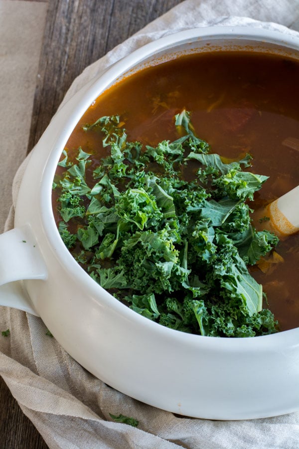 Adding fresh kale to a slow cooker with lentil and minestrone soup.