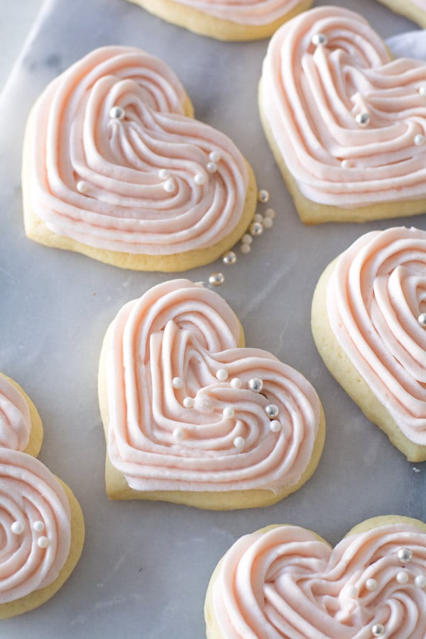 Heart shaped out sour cream sugar cookies with pink cream cheese frosting and drageé.