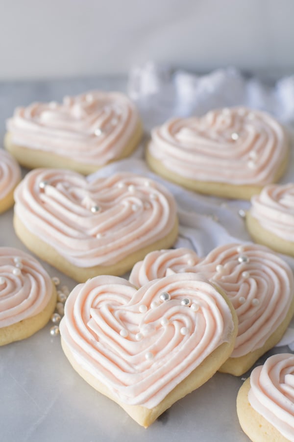 Heart shaped out sour cream sugar cookies with pink cream cheese frosting and drageé.