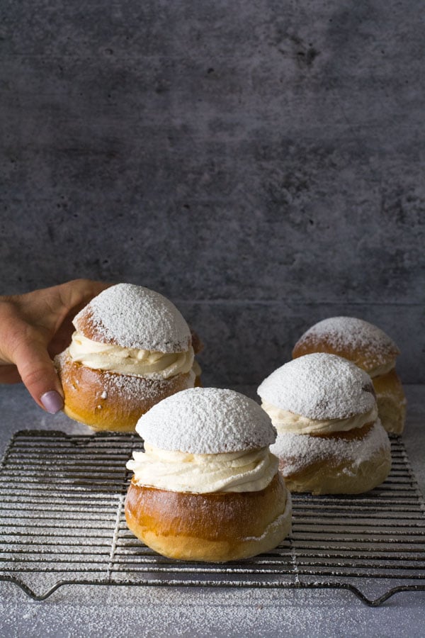 Hand placing a fourth Swedish Semla on a wire baking rack with other buns.