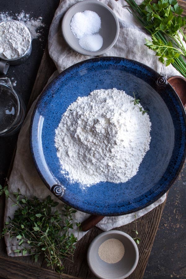 blue bowl with flour on a bread board with green herbs at the side