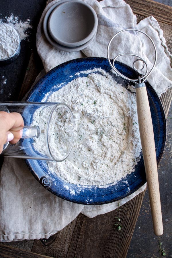 water pouring into blue bowl of flour mixture