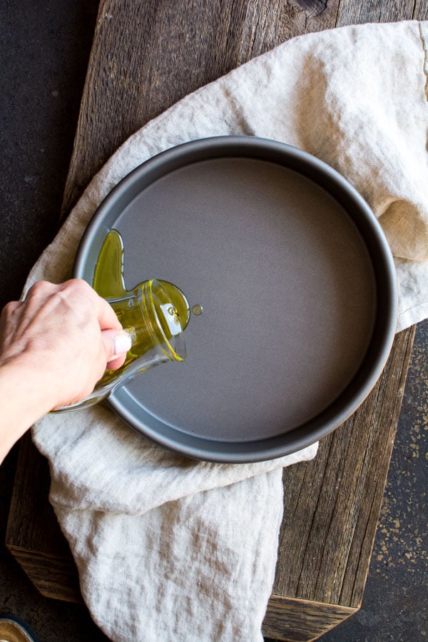 Olive oil pouring into round baking pan