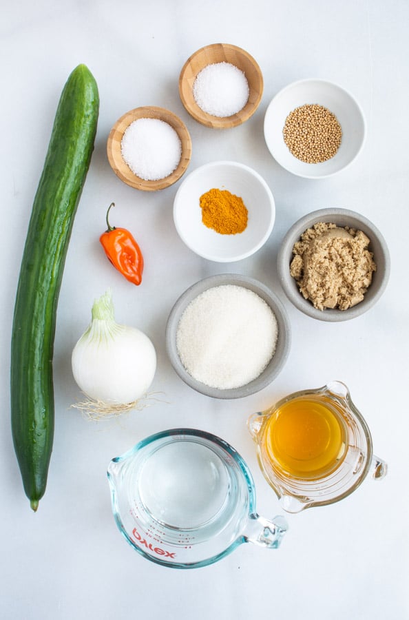 ingredients for pickles, one long cucumber, habanero pepper, brown and white sugar, vinegars in measuring cups