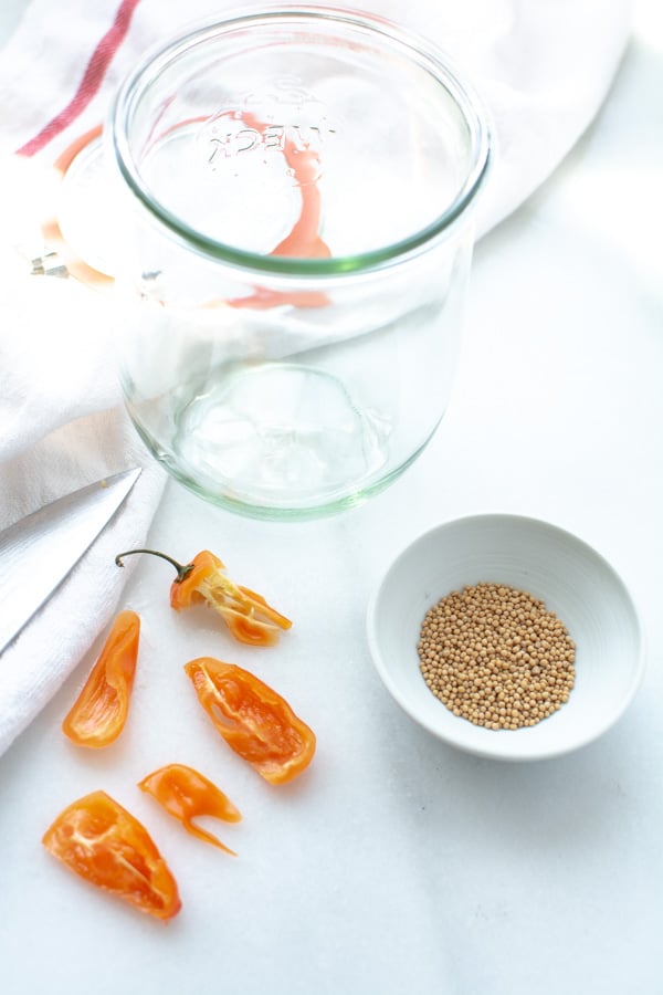 large clear jar with sliced habanero and mustard seeds in a wooden bowl