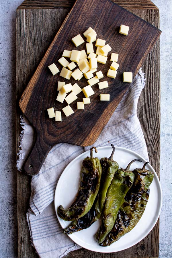 Cubed white cheddar on cutting board next to plate of roasted green chiles