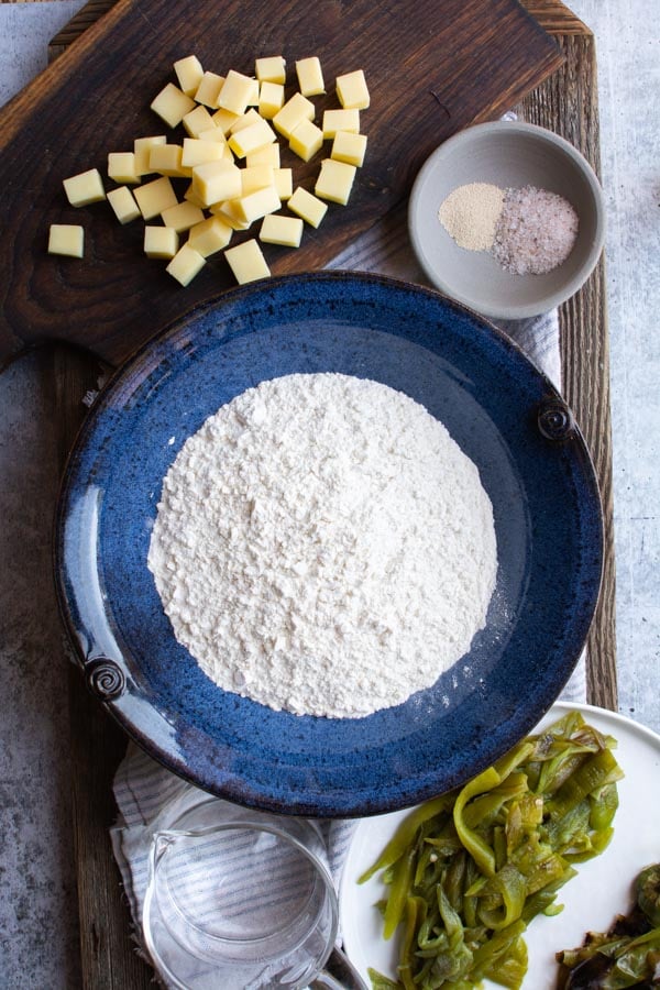 white flour in a blue bowl next to chunks of cheddar and roasted green chiles