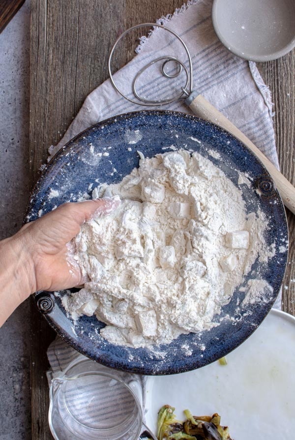 A hand mixing flour, cheddar cheese, and green chiles in blue bowl