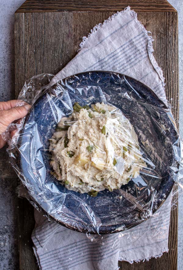 plastic wrap covering blue bowl with cheddar chile bread dough