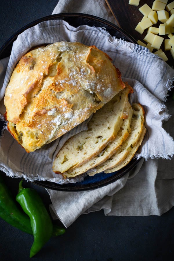 Partially sliced No-Knead Green Chile Cheddar Bread on tan cloth