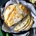 Partially sliced No-Knead Green Chile Cheddar Bread on tan cloth in blue bowl