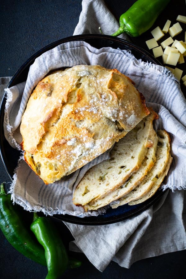 Partially sliced No-Knead Green Chile Cheddar Bread on tan cloth in blue bowl