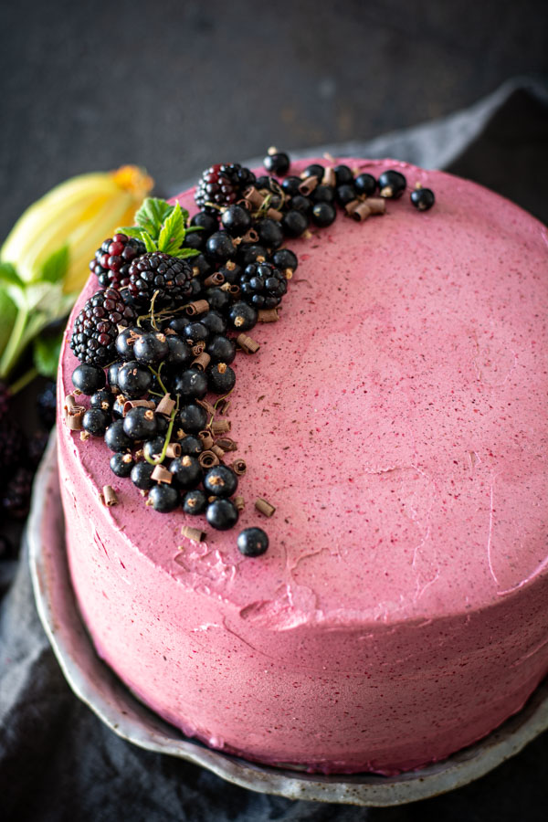 overhead shot of layered cake with hibiscus icing topped with blackberries and black currants