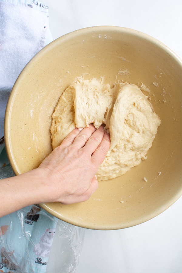 Hand punching down Easter bread dough in yellow bowl.