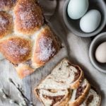 Top down Easter bread with chocolate and pecan swirls. Brioche loaf is cut in half, with one half solid and the other cut into two slices. Gray bowls with pink and blue eggs are to the side for decoration.