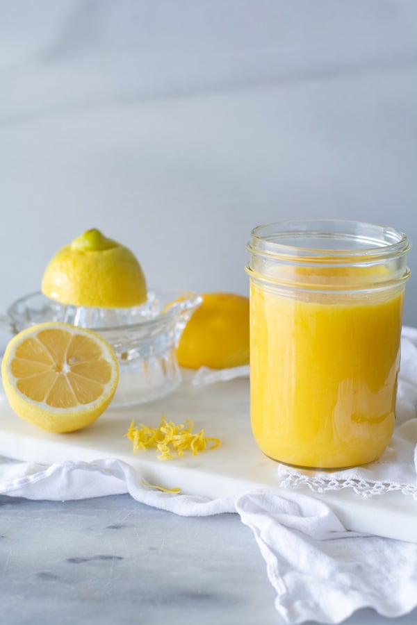 jar of lemon curd on white cloth with fresh lemons in background