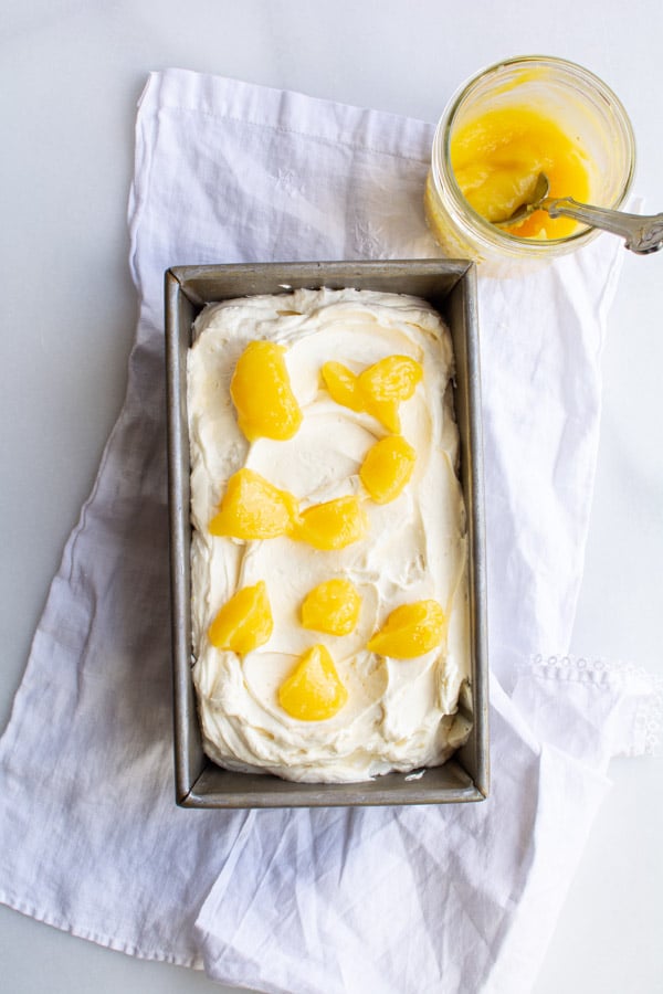 No-churn lemon curd ice cream in a bread pan dotted with lemon curd