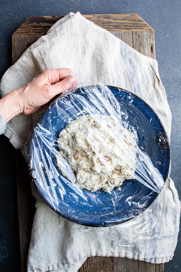 Plastic wrap over blue bowl filled with dough