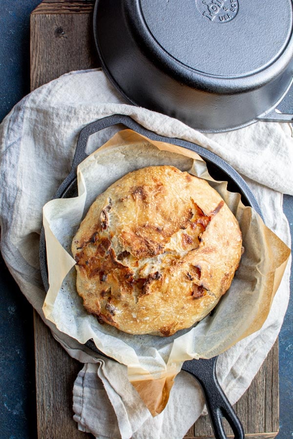 Baked white chocolate pecan crusty bread on parchment paper in a cast iron pot